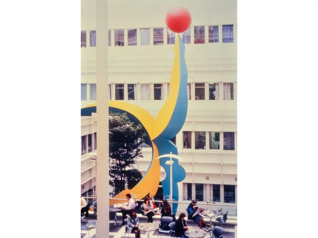 A tall blue and yellow steel acrobat balances a red sphere inside the Chelsea and Westminster Hospital atrium.