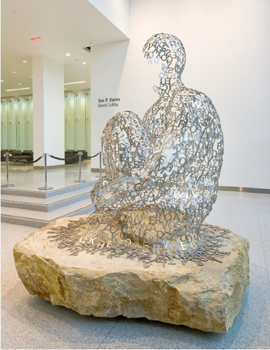 A seated figure made from stainless steel letters rests on a large stone inside Cleveland Clinic.