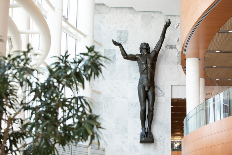 A monumental bronze man with raised arms is mounted inside the Mayo Clinic atrium.