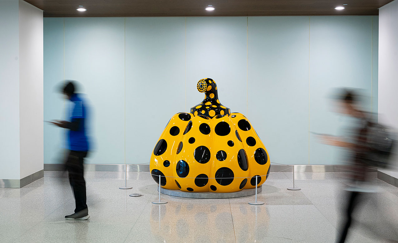 A yellow pumpkin covered in black dots stands in a Cleveland Clinic lobby as visitors pass.
