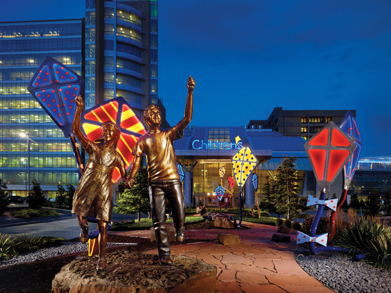 Bronze children fly brightly coloured illuminated kites outside the Children’s Hospital in Oklahoma City at night.