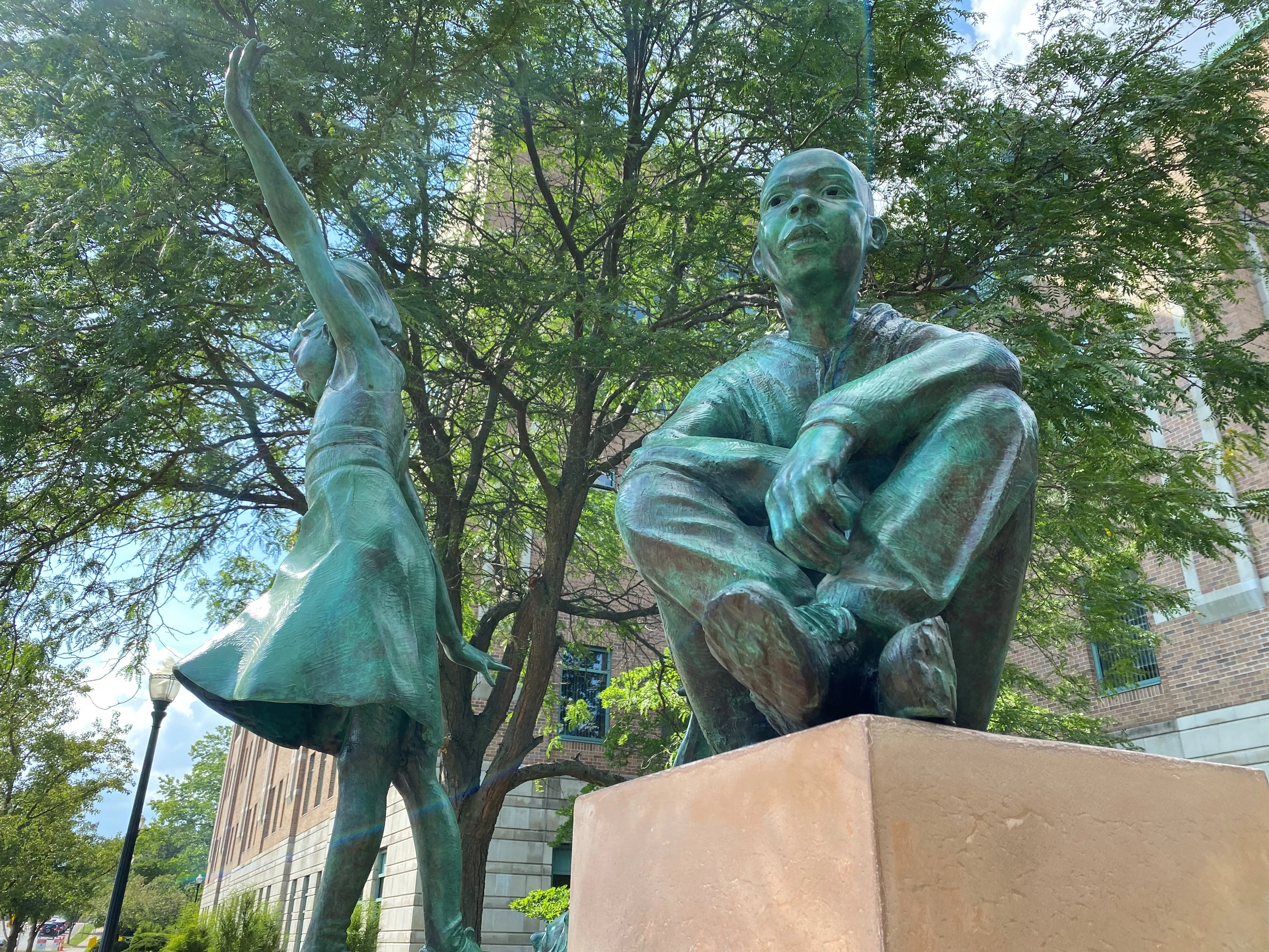 Detail of two bronze children in Josh Diedrich’s sculpture outside Bronson Children’s Hospital, one seated and one raising a hand.