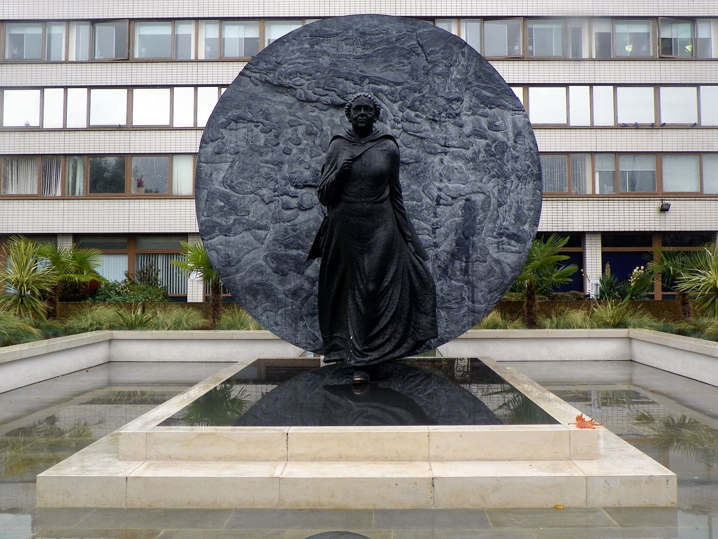 Bronze statue of Mary Seacole striding forward in front of a large bronze disc outside St Thomas’ Hospital.