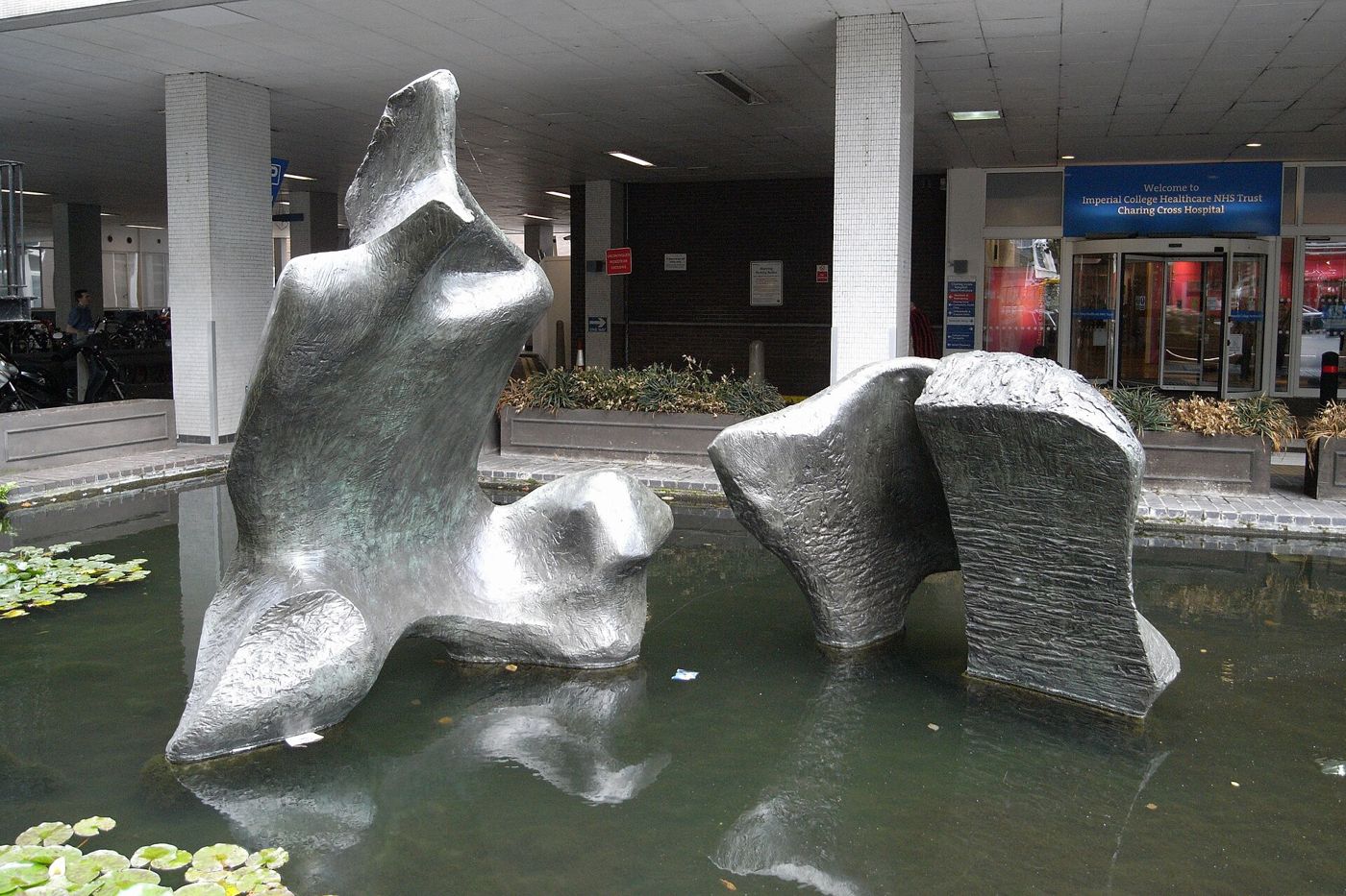 Two large bronze forms of Henry Moore’s reclining figure stand in a shallow pool at the entrance of Charing Cross Hospital.